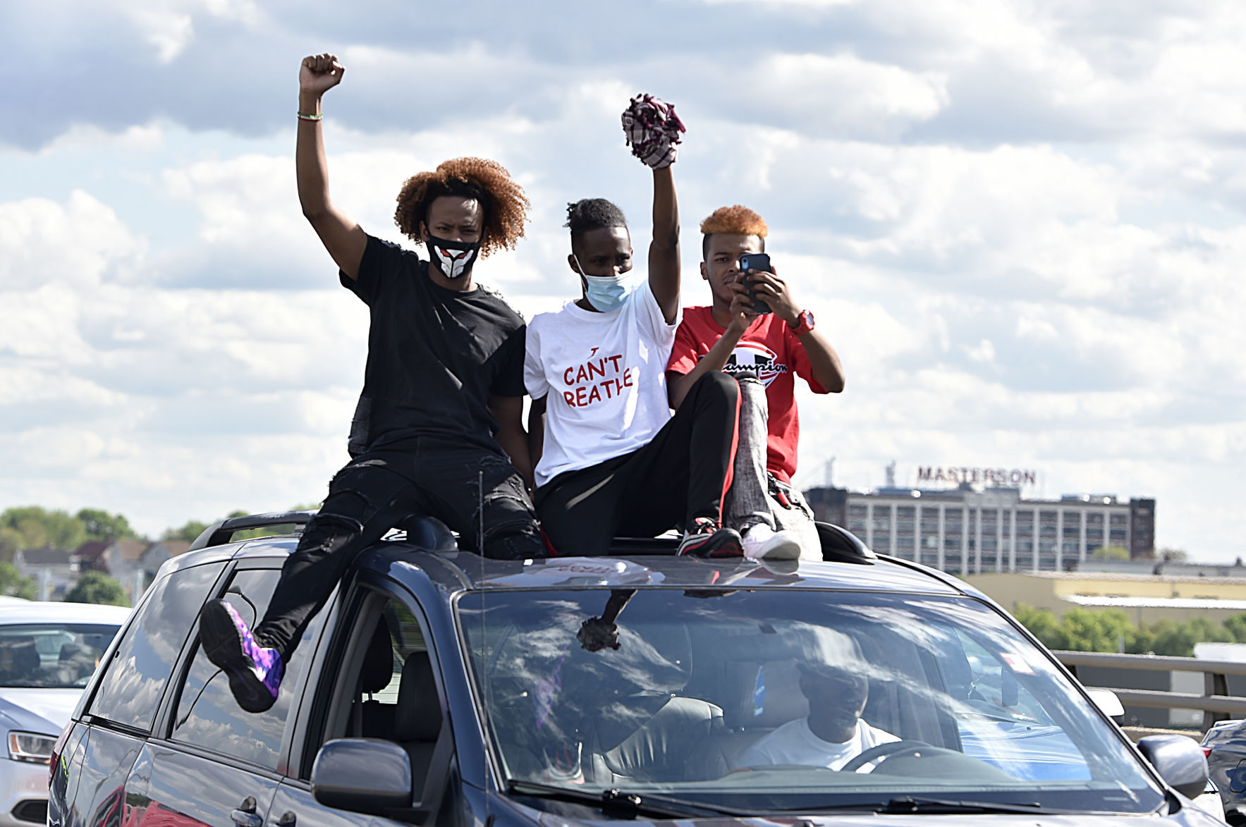 Young men ride on top of a slow-moving vehicle during the protest